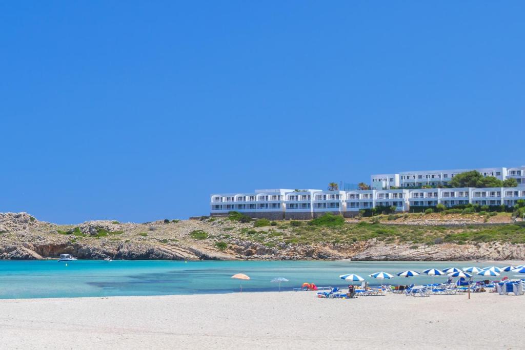a beach with chairs and umbrellas in front of a hotel at Beach Club Menorca in Son Parc