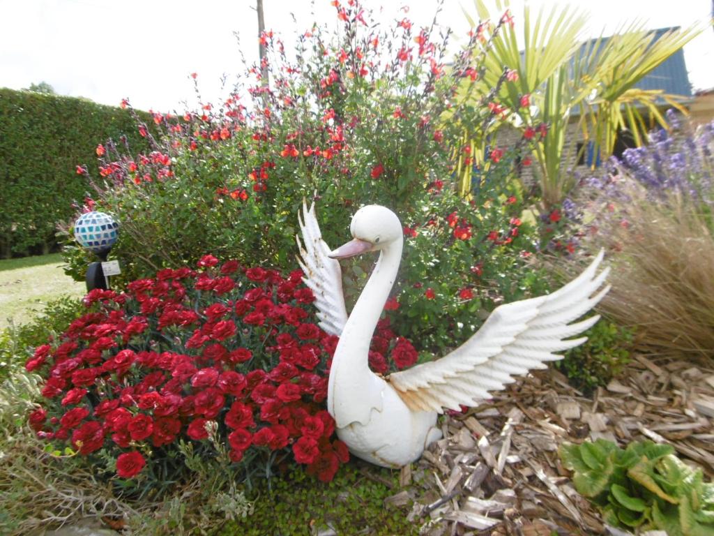 una statua di cigno bianco in un giardino fiorito di Chambre d'hotes de la Mousse a Saint Remy sur Orne