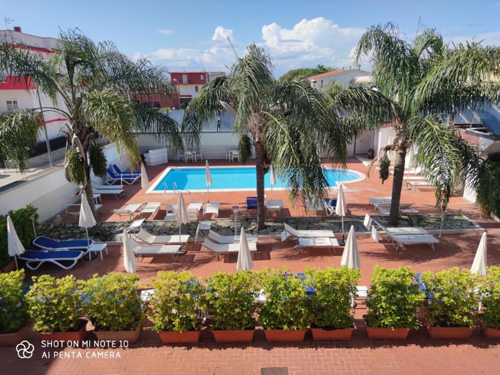 un complexe avec une piscine, des chaises longues et des palmiers dans l'établissement Hotel Resort Il Panfilo, à Lago Patria
