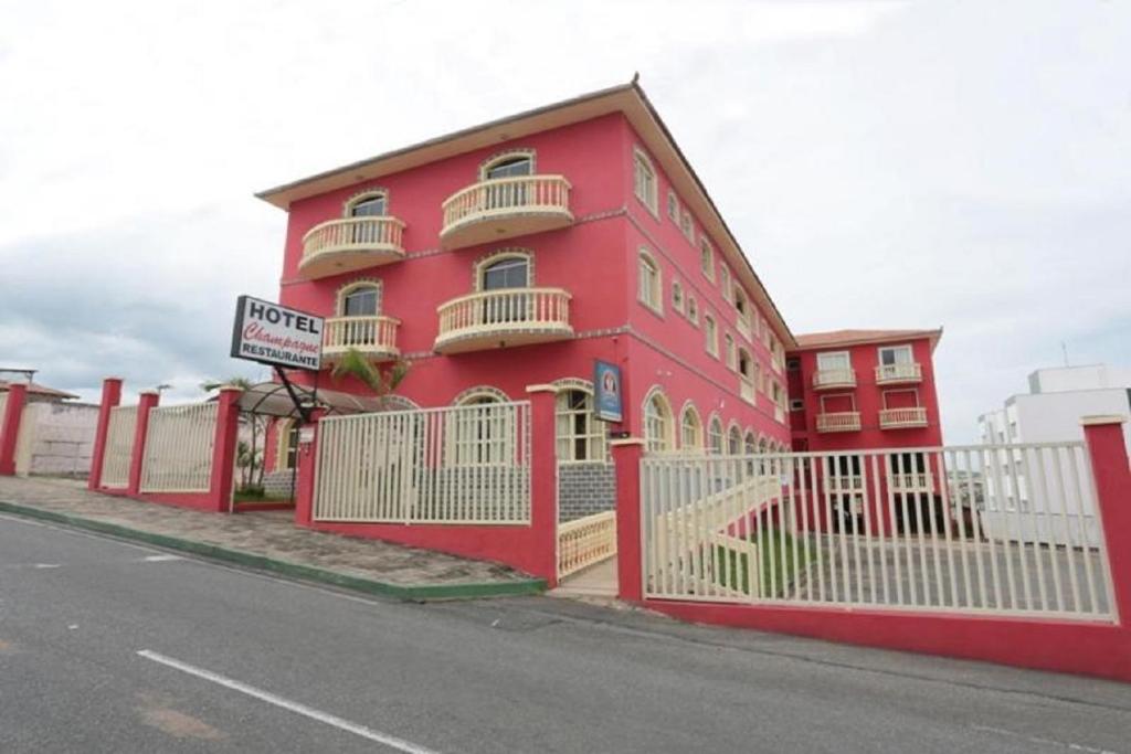 a red building with a white fence next to a street at Hotel e Restaurante Champagne in Campo Belo
