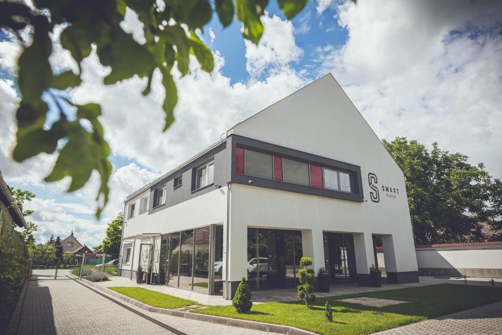 a white building with red windows on a street at Smart Hotel in Körösladány