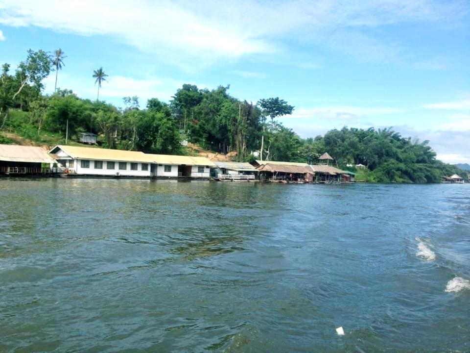 um barco na água com casas na costa em แพแหม่มทัวร์ em Sai Yok