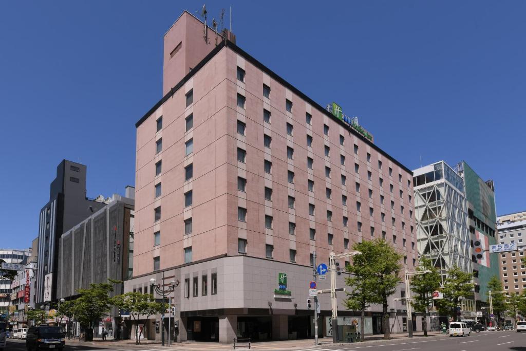 un grand bâtiment rose dans une rue de la ville dans l'établissement ANA Holiday Inn Sapporo Susukino, an IHG Hotel, à Sapporo
