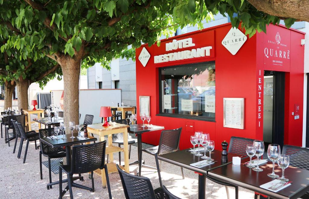 a restaurant with tables and chairs in front of a red wall at Le Quarré Hôtel Bistrot in Bruguières
