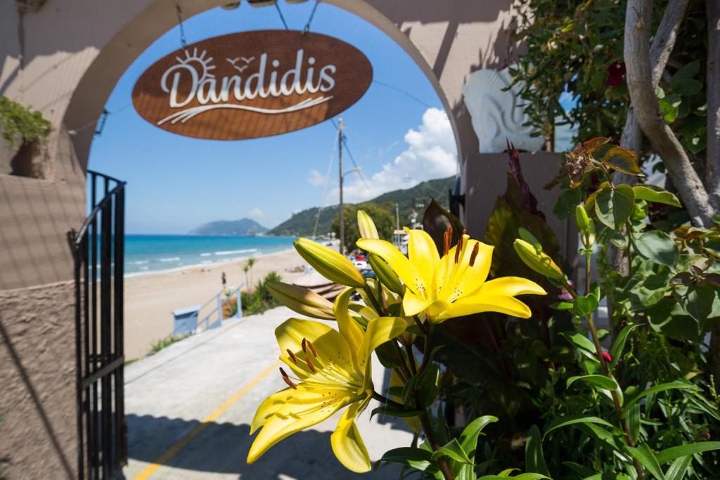 a yellow flower in front of a sign with a beach at Dandidis Seaside Pension in Agios Gordios