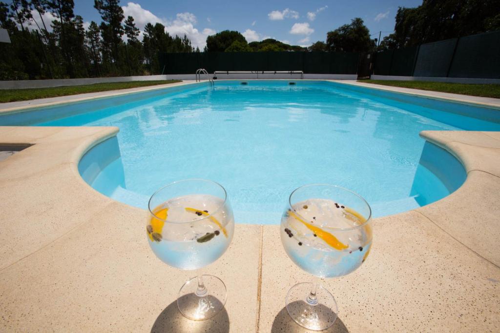 two wine glasses with fish in them next to a swimming pool at Sossego da Natureza - Monte Alentejano in Grândola