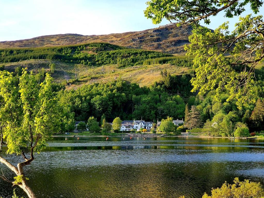 a lake in front of a mountain with a house at Achray House Restaurant with Rooms in Saint Fillans