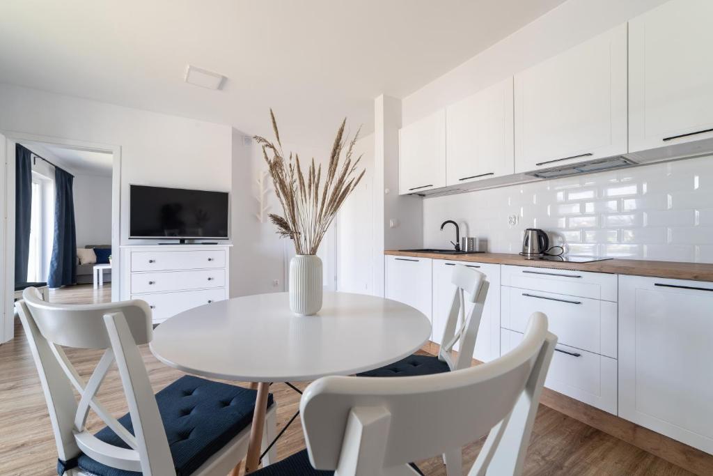 a white kitchen with a white table and chairs at Apartamenty Białe Piaski in Jastarnia
