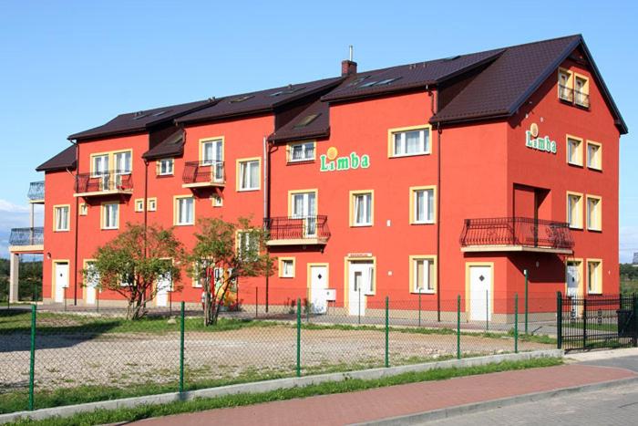 un grand bâtiment rouge avec une clôture devant lui dans l'établissement Limba, à Łeba