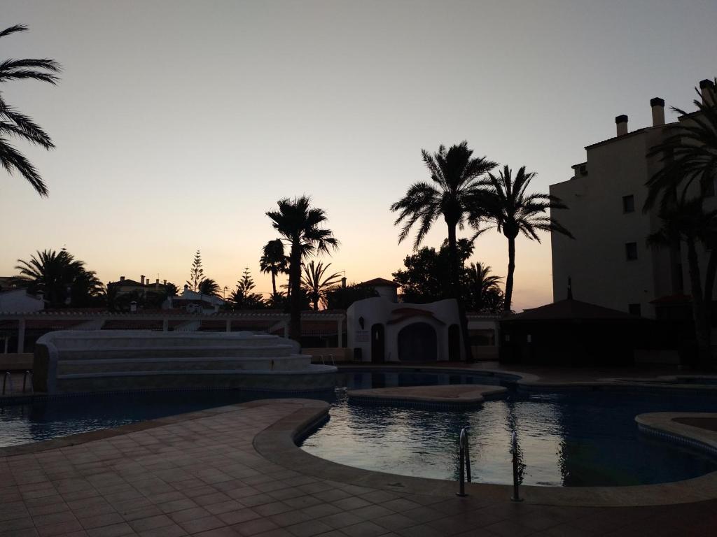 a pool with palm trees and a sunset in the background at Estudio Caballo-Piscina in Denia