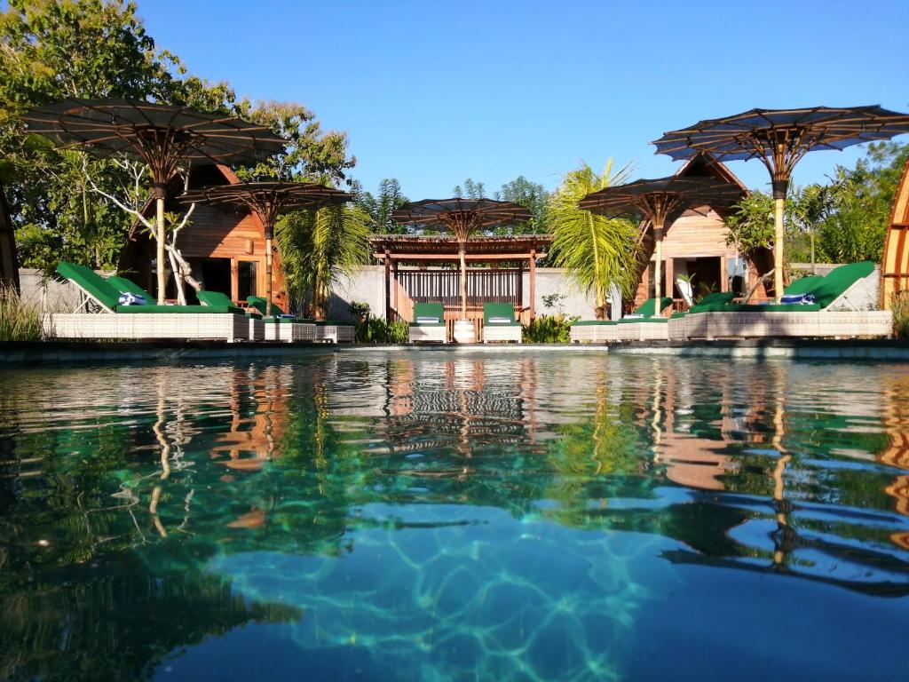 a pool of water with trees and umbrellas at Lumbung Bukit Resort Uluwatu in Uluwatu