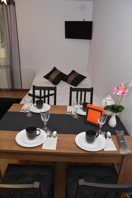 uma mesa de madeira com pratos e copos e uma cama em Apartamenty Kometa em Biała Podlaska