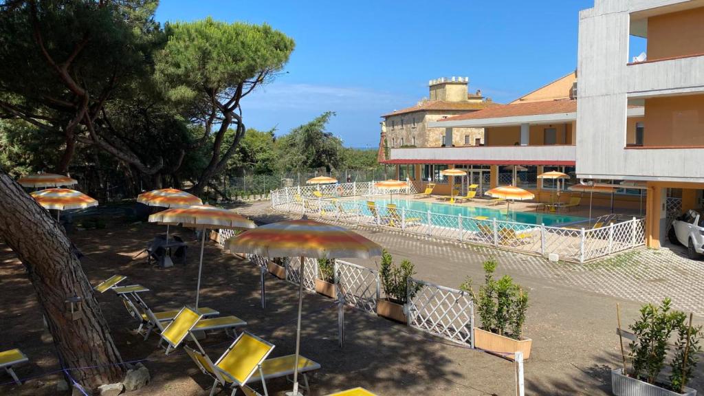 eine Gruppe von Stühlen und Sonnenschirmen neben einem Pool in der Unterkunft Hotel Paradiso Verde in Marina di Bibbona