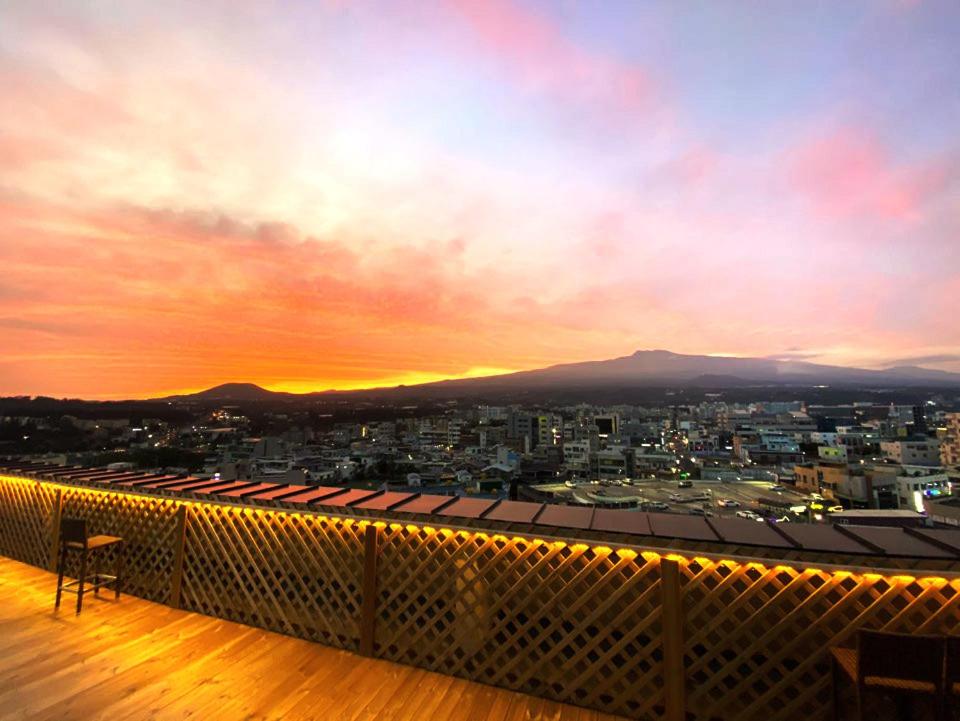 einen Balkon mit Blick auf eine Stadt bei Sonnenuntergang in der Unterkunft Hotel Rest Seogwipo in Seogwipo