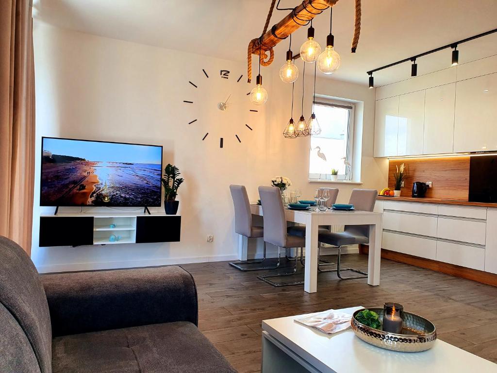 a living room with a table and a clock on the wall at "Golden Sand & Sea" - Nowoczesny apartament w Kołobrzegu 47m2 in Kołobrzeg