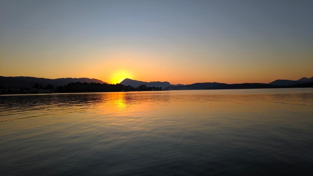 una puesta de sol sobre un cuerpo de agua con montañas en el fondo en Poros Mood, en Poros