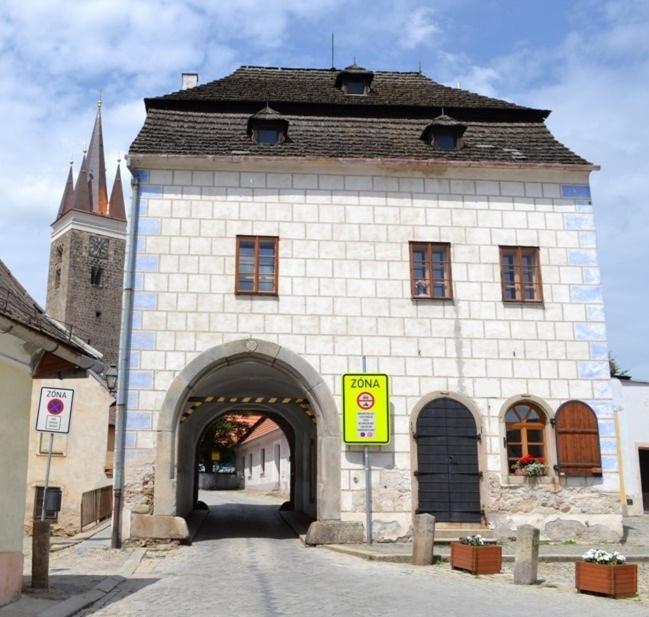 un grand bâtiment en briques avec une arche et une église dans l'établissement Apartmán Horní Brána, à Telč