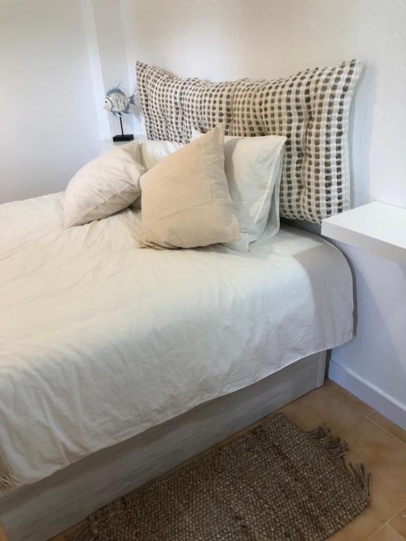 uma cama com lençóis brancos e almofadas em Espectacular apartamento con piscina en Calella de Palafrugell em Calella de Palafrugell