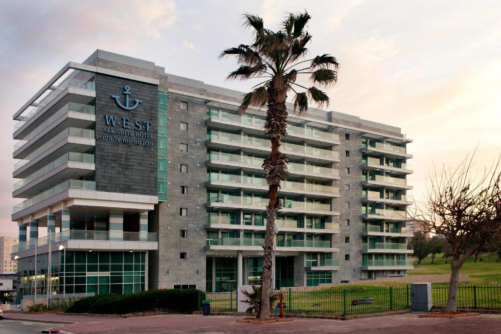 ein Gebäude mit einer Palme davor in der Unterkunft West All Suites Hotel Ashdod in Aschdod