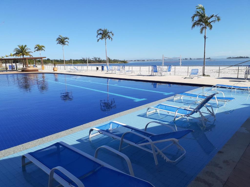 uma piscina com cadeiras e a praia em Apartamento Condomínio Golden Lake Arraial do Cabo - RJ em Arraial do Cabo