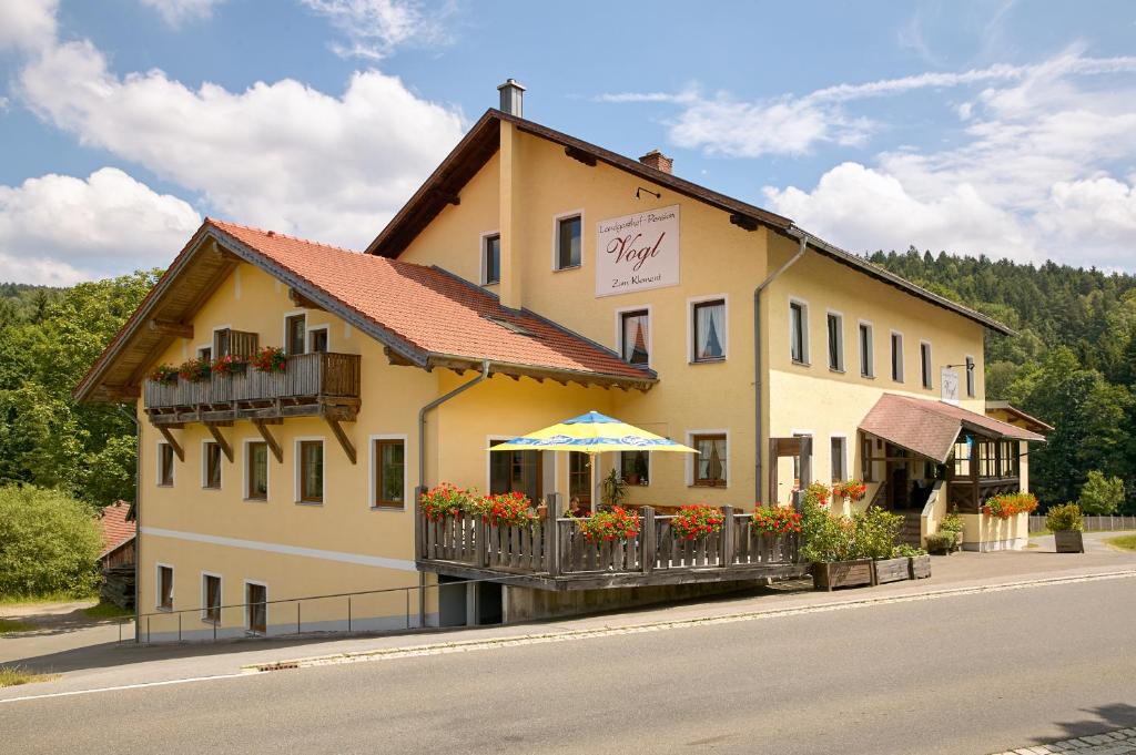 a yellow building with a balcony and an umbrella at Landgasthof Vogl - Zum Klement in Neukirchen beim Heiligen Blut