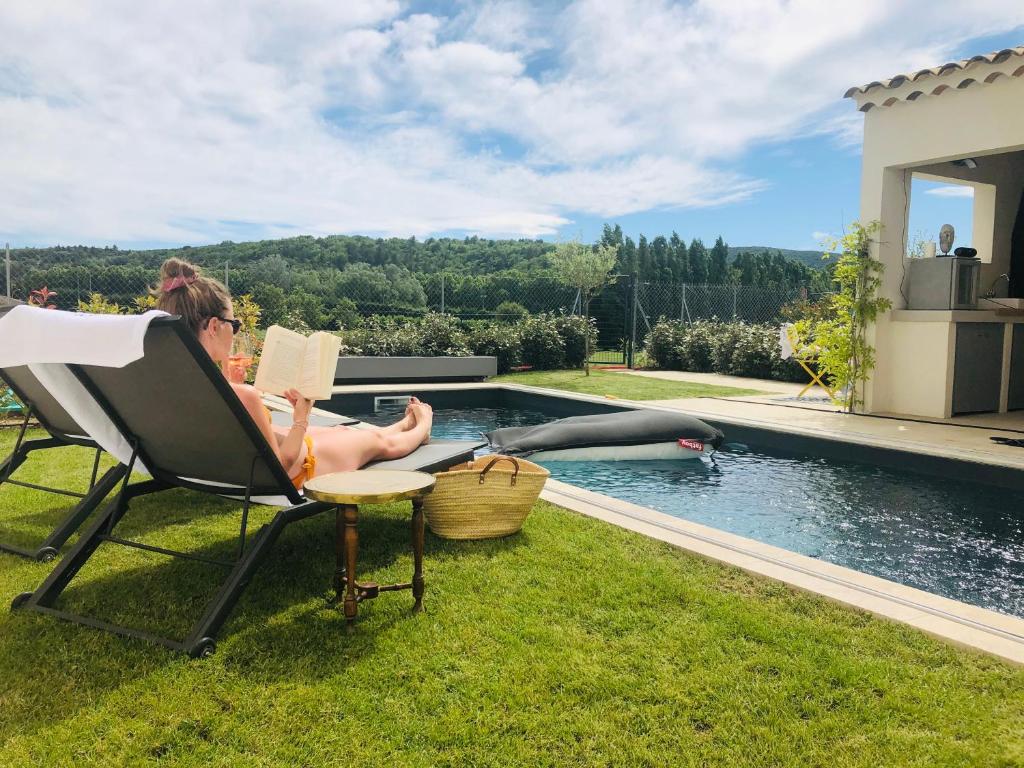 a woman sitting in a chair next to a swimming pool at La Maison d AME - for the perfect stay at the Mont Ventoux in Malaucène