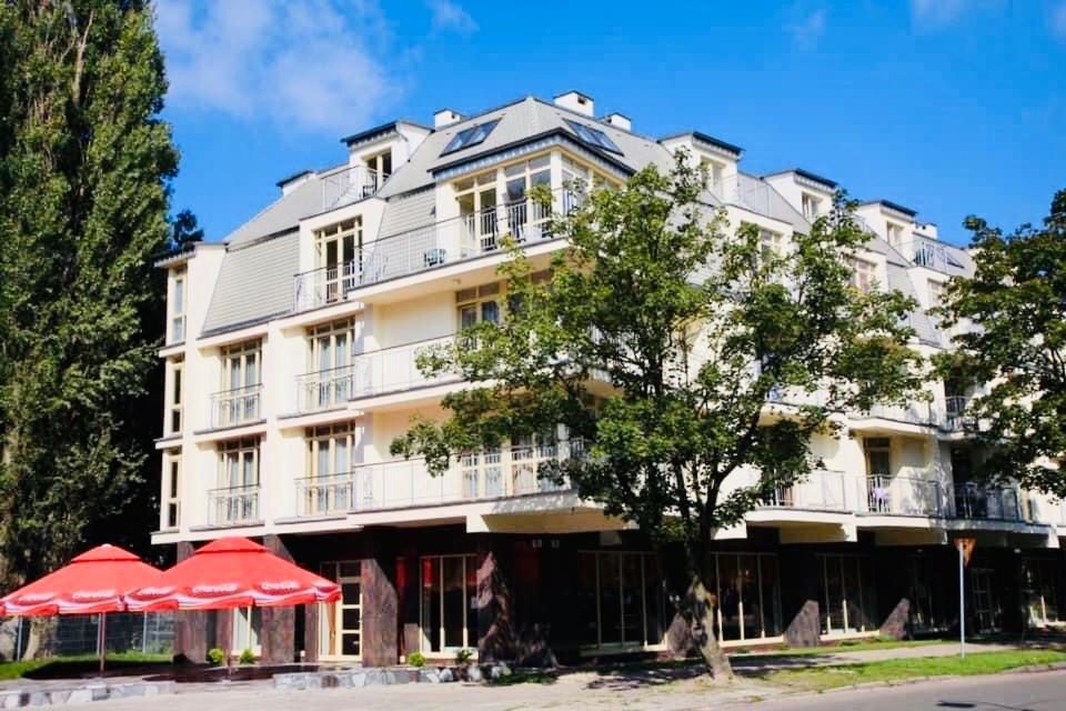 duży biały budynek z czerwonymi parasolami przed nim w obiekcie Apartament w dzielnicy nadmorskiej (hotel Arstone) w Świnoujściu