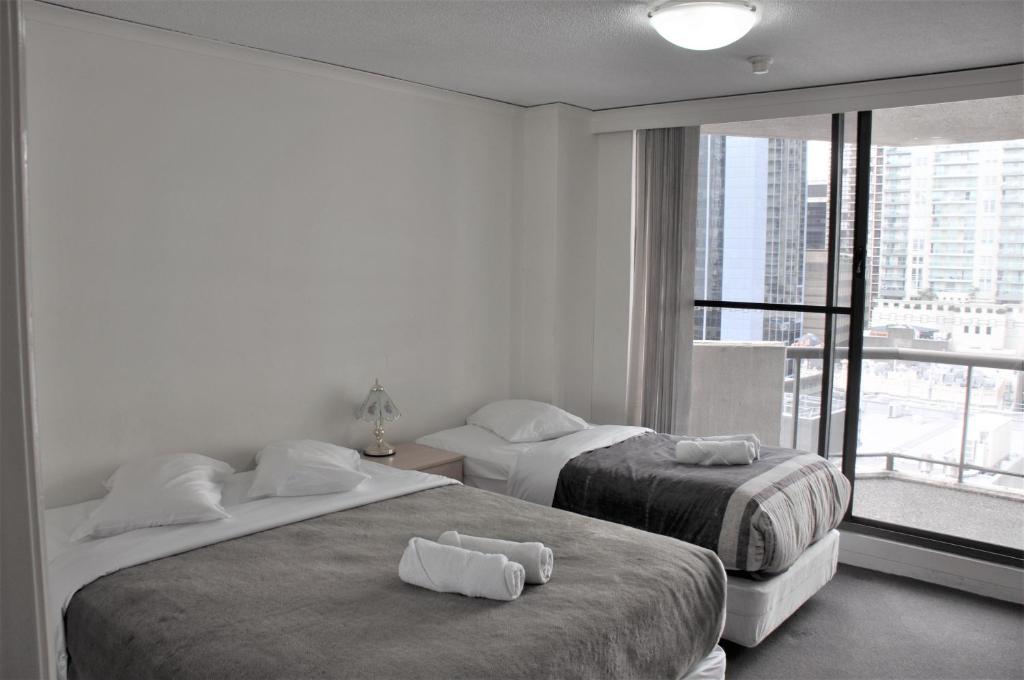 two beds in a room with a large window at Accommodation Sydney City Centre - 2 Bedroom Apartment with Balcony on Top Floor in Sydney