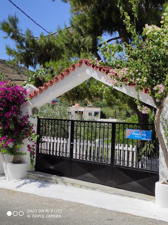 a black fence with a white arch and pink flowers at Vokamvilia Apartments in Kini