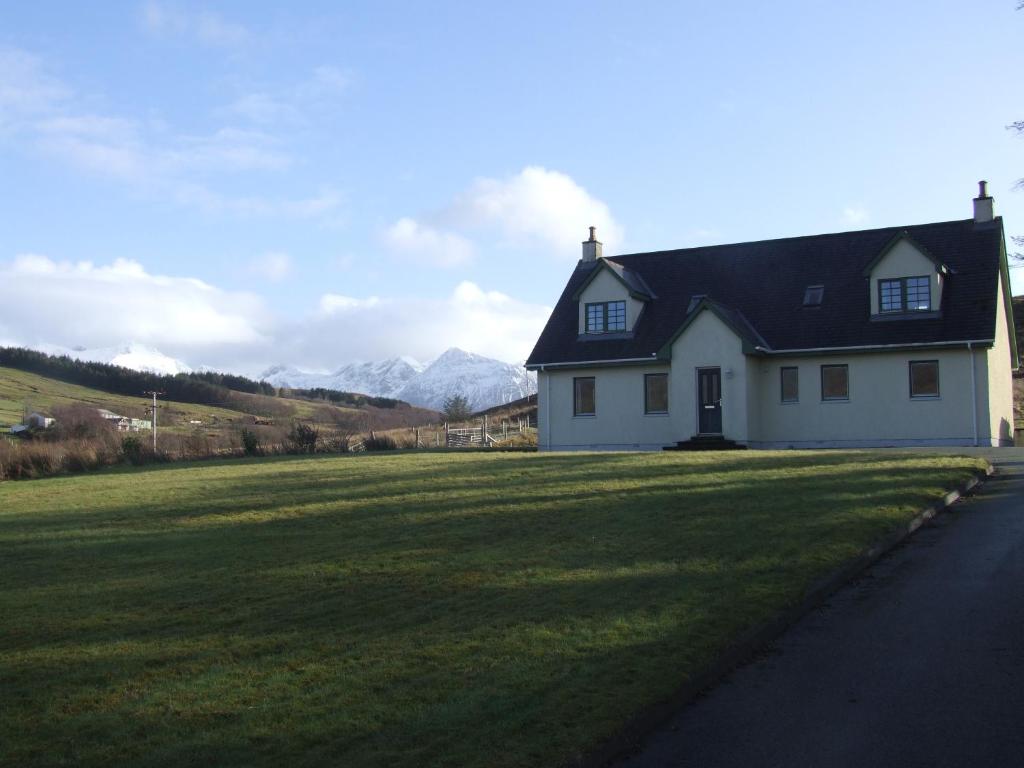 a white house with a black roof on a grass field at Trien Lodge in Carbost