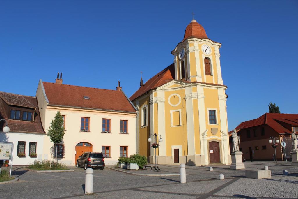 a yellow building with a clock tower in a street at Apartmán U Kostela in Veselí nad Moravou