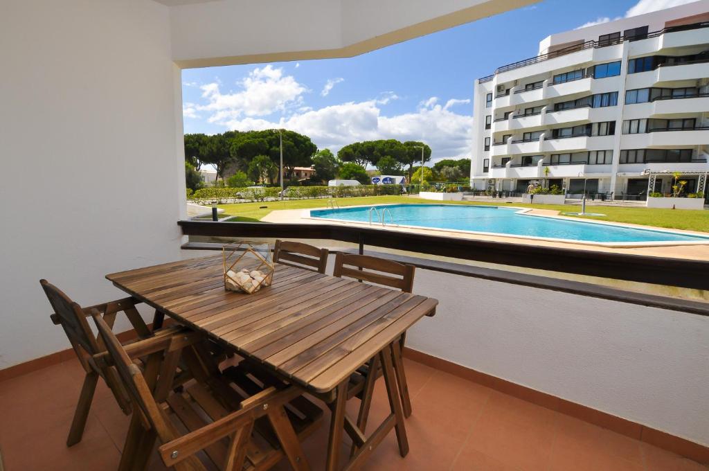 a balcony with a wooden table and chairs and a swimming pool at Tenis Golf Mar by OCvillas in Quarteira