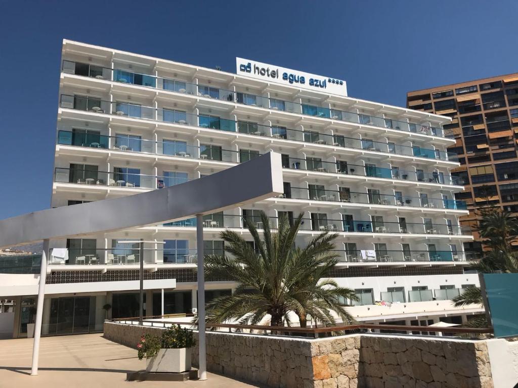 a large white building with a palm tree in front of it at Hotel Agua Azul - Adults Only in Benidorm