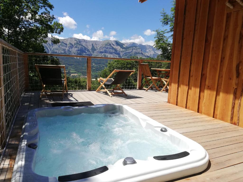 a hot tub on a deck with a view of mountains at Ma Cabane des Hautes-Alpes in Saint-Julien-en-Champsaur
