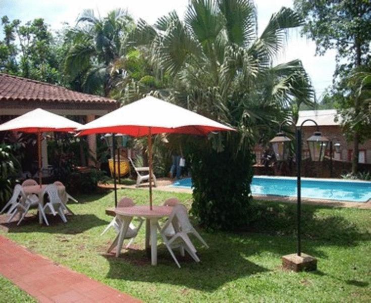einen Tisch und Stühle mit Sonnenschirmen neben einem Pool in der Unterkunft El Guembe Hostel House in Puerto Iguazú