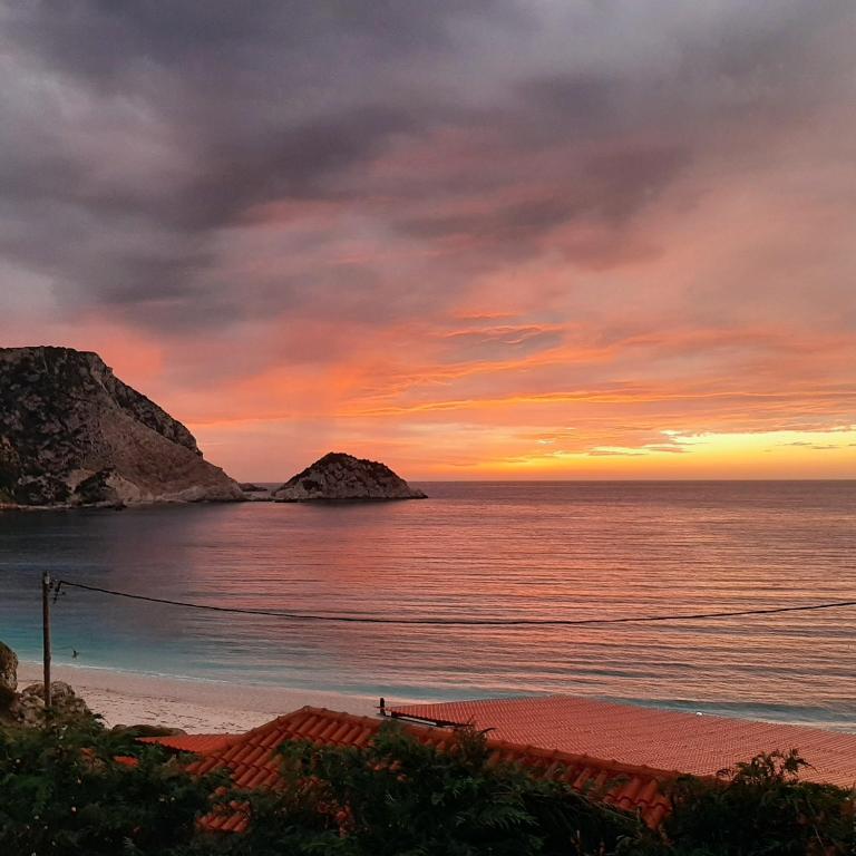 a sunset on the beach with rocks in the water at Petani Beachside Accommodation in Vóvikes