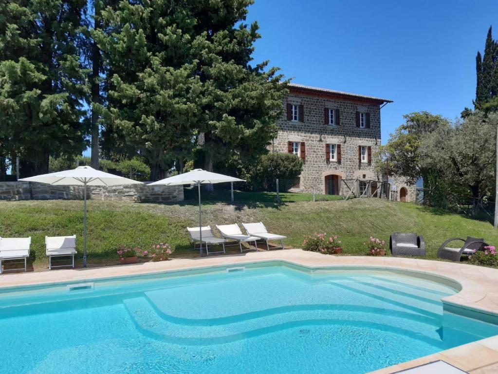 a swimming pool with chairs and umbrellas and a building at Antica Residenza Montereano in Gubbio