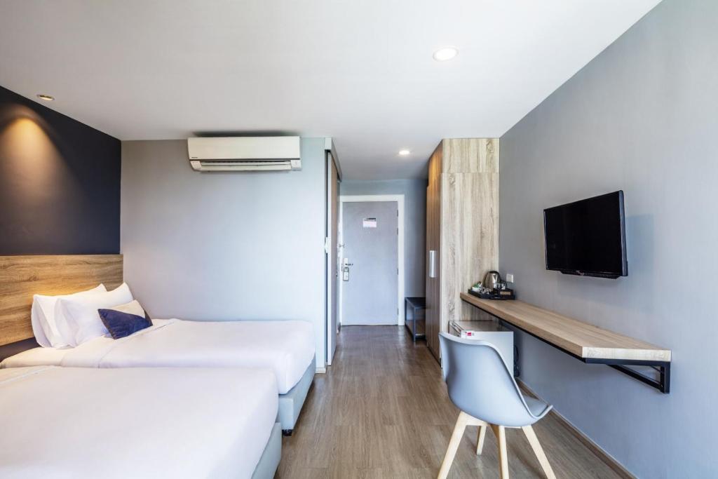 A compact twin room with two beds, a wall-mounted TV, desk, kettle and mini-fridge.
