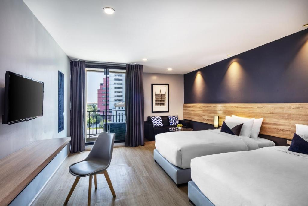 A two-bed room with a desk, TV, sofa corner and balcony doorway.