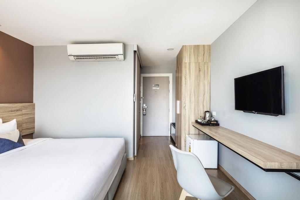 A bedroom corner with a bed, television, desk, chair and air conditioner.