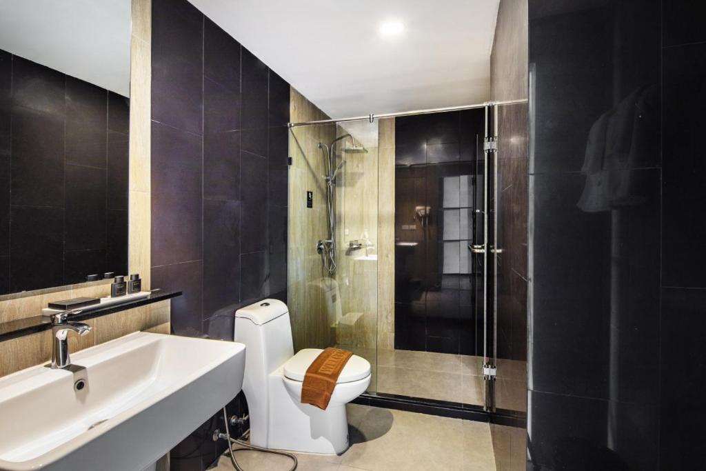 A dark-tiled bathroom combines a wide vanity, toilet and enclosed glass shower.