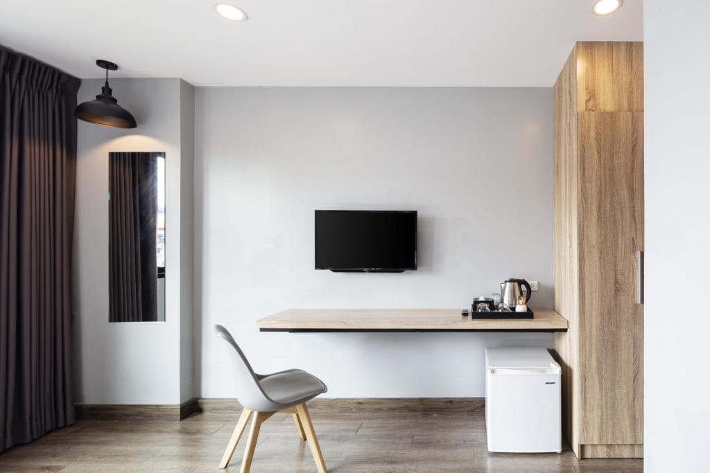 A compact in-room work area with a wall-mounted TV, desk, chair, kettle and mini-fridge.