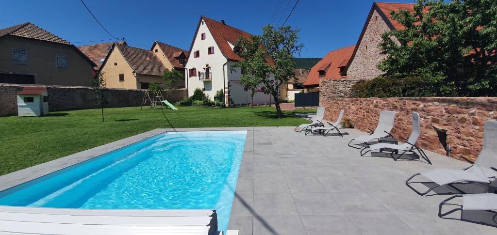 a swimming pool with chairs and a yard with houses at La Maison d'Emilie in Pfaffenheim