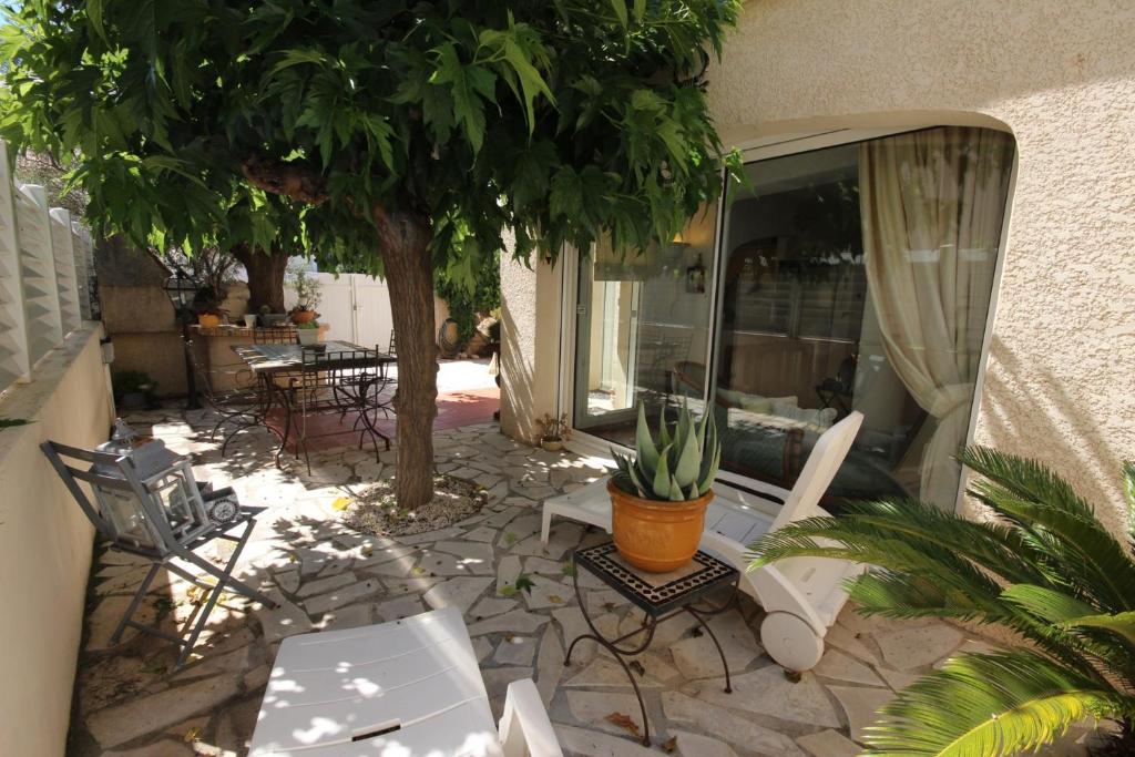 un patio con sillas, mesas y un árbol en Bel Appartement climatisé de plain pied 80m de la mer grand séjour 2 chambres belle terrasse LXRM3, en Portiragnes