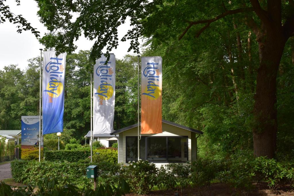 un edificio con banderas delante de un árbol en Heidepark Veluwschkarakter, en Vierhouten