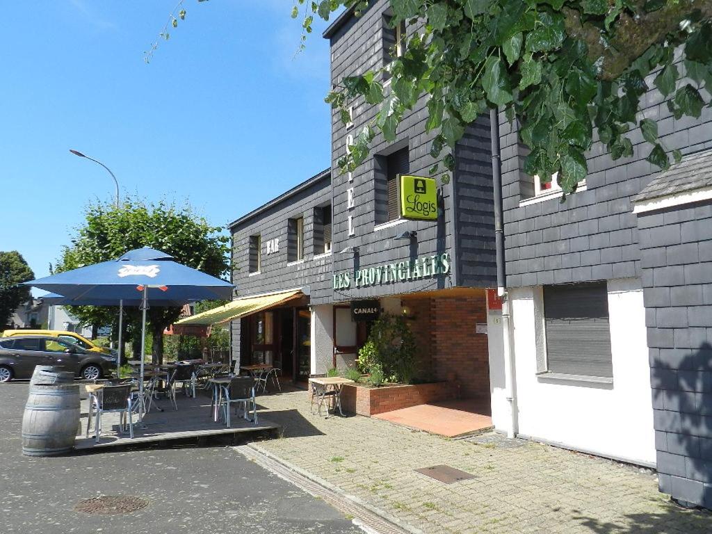 - un bâtiment avec une table, des chaises et un parasol dans l'établissement Logis Les Provinciales, à Arpajon-sur-Cère