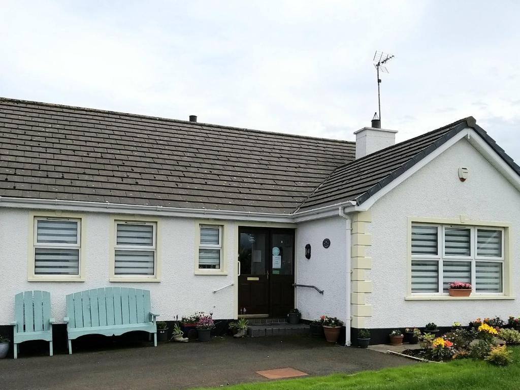 a white house with two blue benches in front of it at Braeside B&B in Bushmills