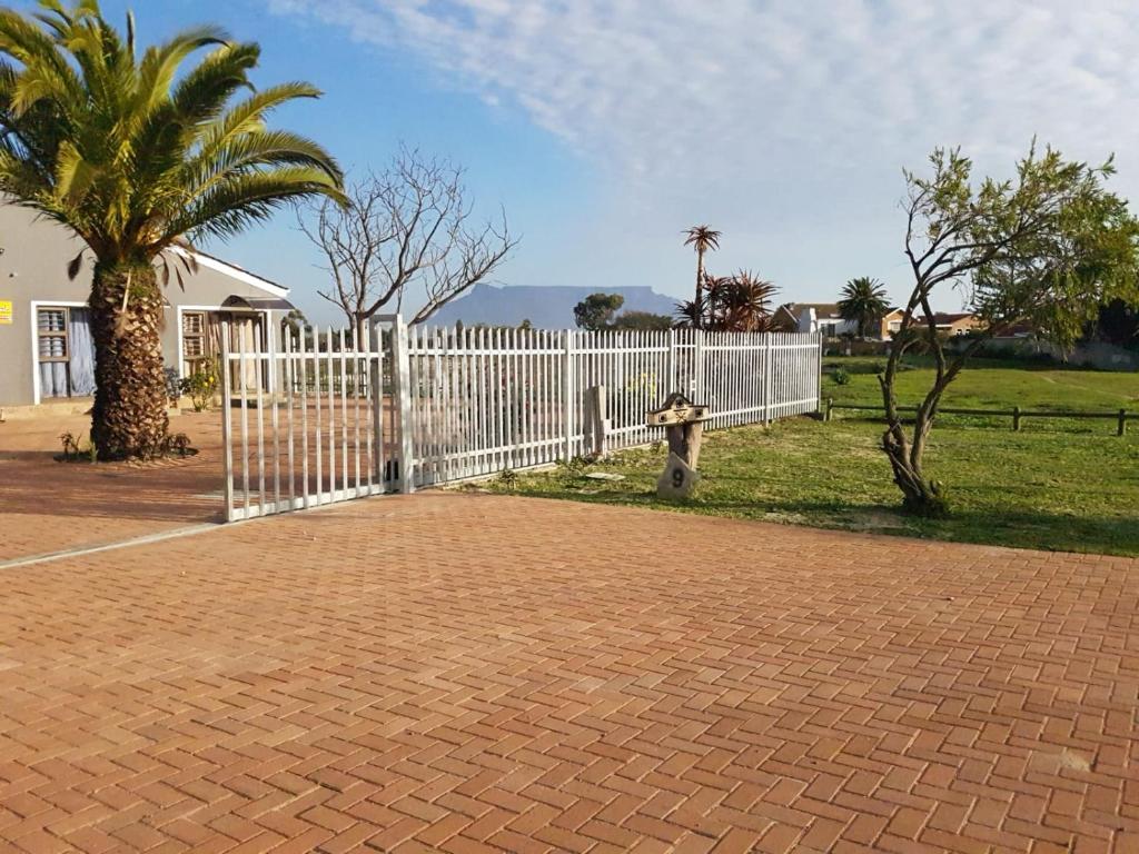 a white fence with a palm tree next to a field at Sir James Self Catering in Cape Town