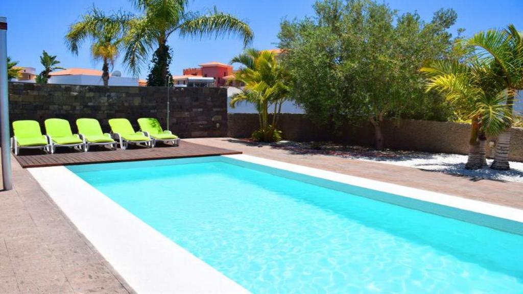 a swimming pool with green chairs next to a fence at Exclusive Villa in Bahia del Duque in Adeje