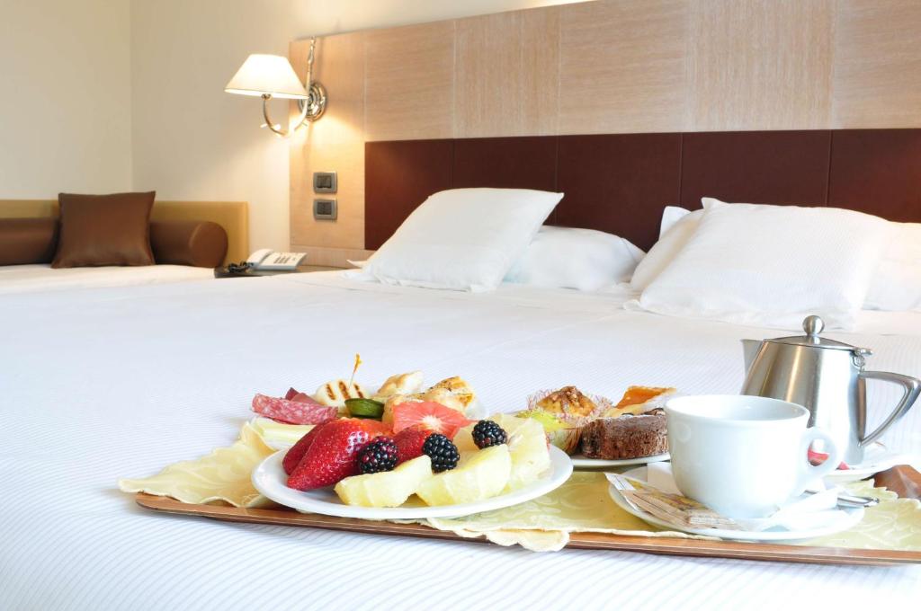 a tray of fruit and a cup of coffee on a bed at San Giorgio, Sure Hotel Collection by Best Western in Forlì
